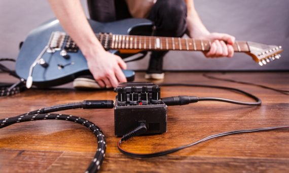 Man with musical instrument setting up guitar audio stomp box effects and cables in music studio