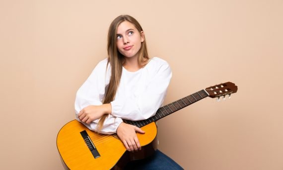Teenager girl with guitar over isolated background making doubts gesture while lifting the shoulders