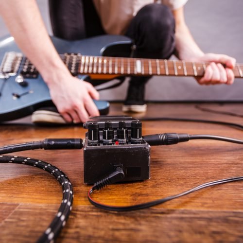 Man with musical instrument setting up guitar audio stomp box effects and cables in music studio