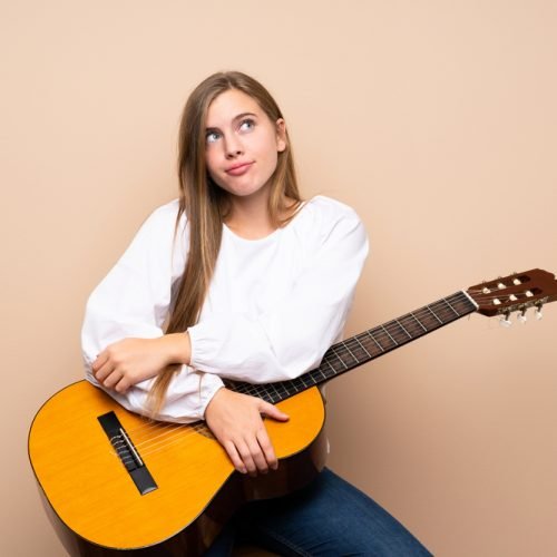 Teenager girl with guitar over isolated background making doubts gesture while lifting the shoulders