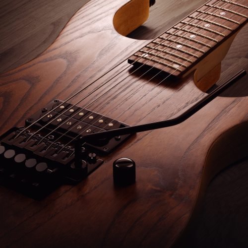 Close up on the body of custom electric guitar with natural finish, selective light on it, wooden background